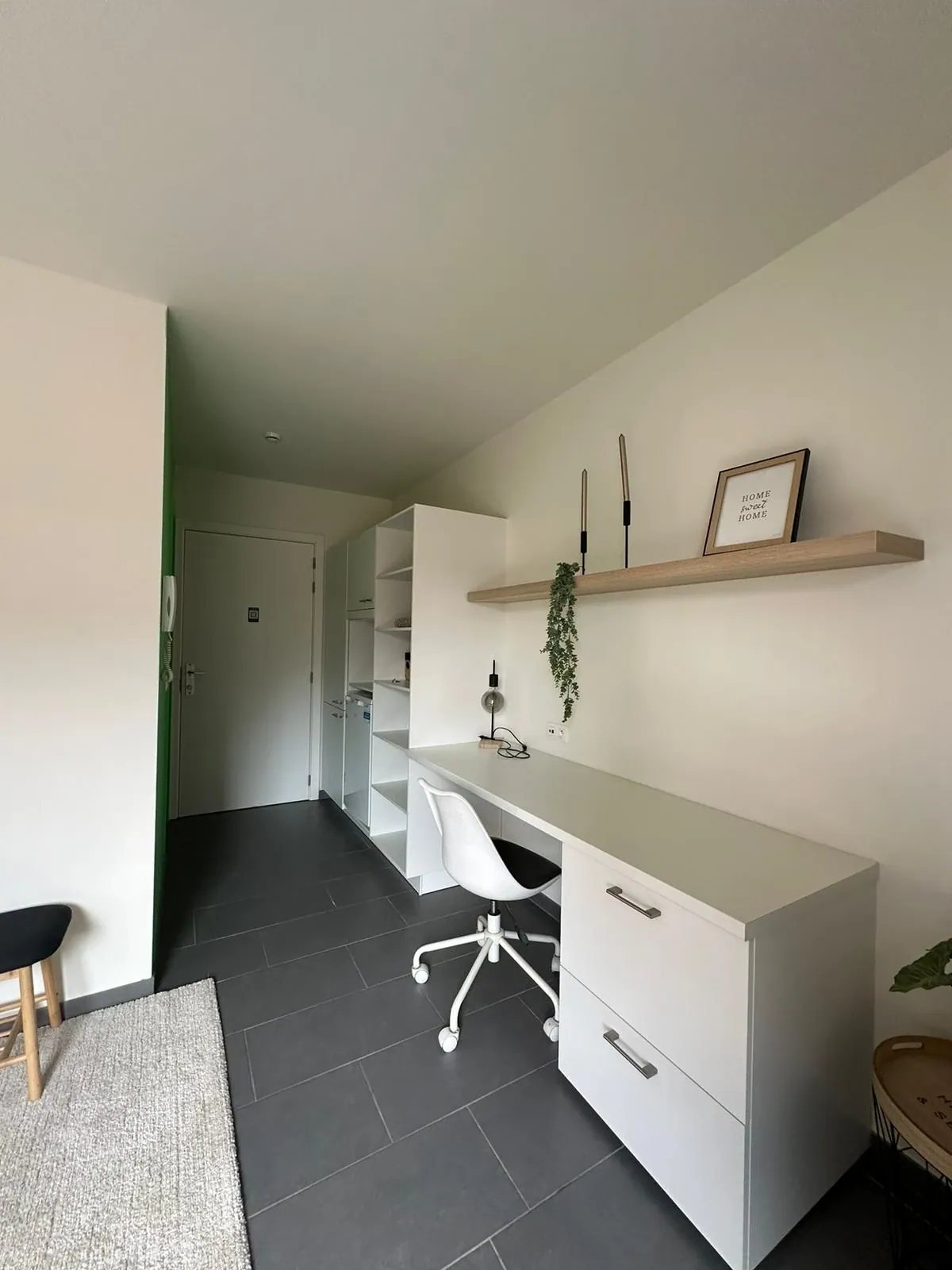 Studentenkamer met bureau, bureaustoel en wandplank naast de inkom met parlofoon