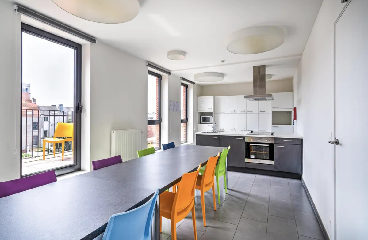 Tweede gemeenschappelijke keuken met lange eettafel en balkondeur